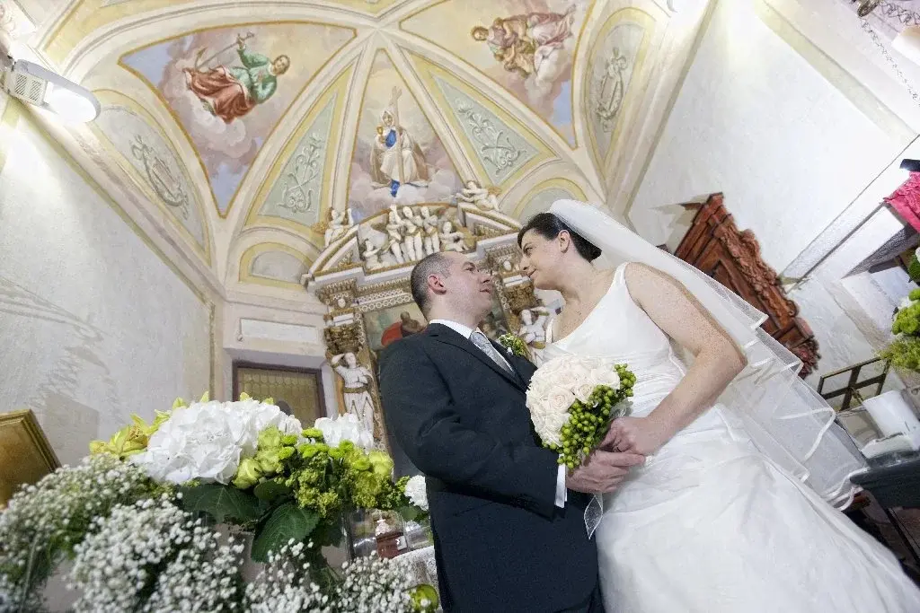 Gli sposi si guardano negli occhi sotto la volta affrescata della chiesa, tra i fiori bianchi